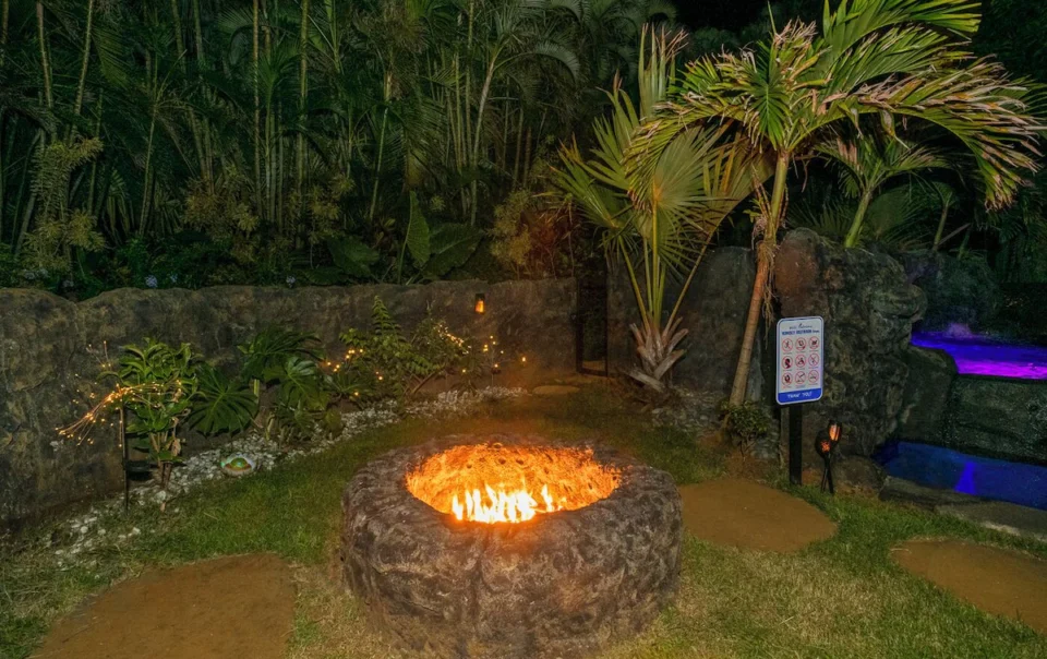 Stone ring fire pit glowing in tropical garden
