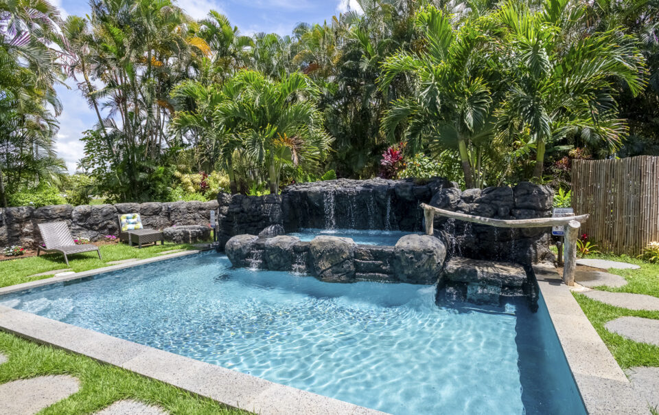 Tropical pool area with waterfall and loungers.