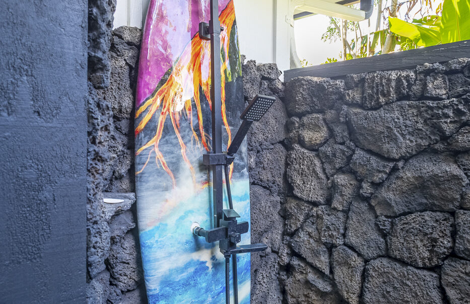 Surfboard shower fixture against stone wall.