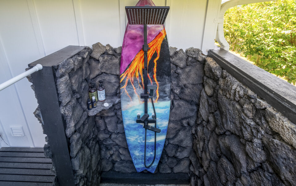 Outdoor shower with surfboard and stone wall.